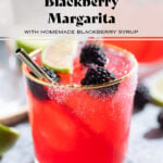 Bright purple red blackberry margarita in a glass with a gold rim garnished with blackberries and lime slices and salt on the rim.