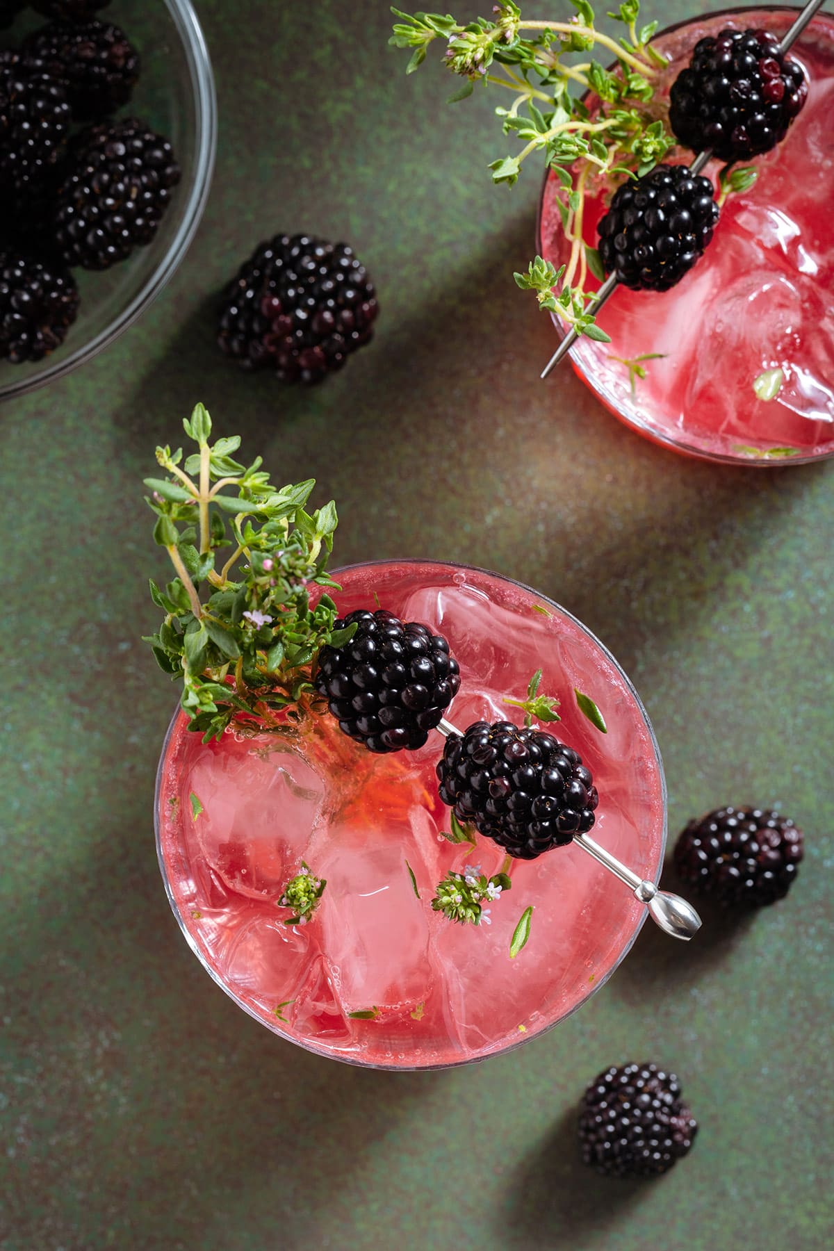 Bright pink red blackberry mocktail in a short glass garnished with blackberries and fresh thyme.