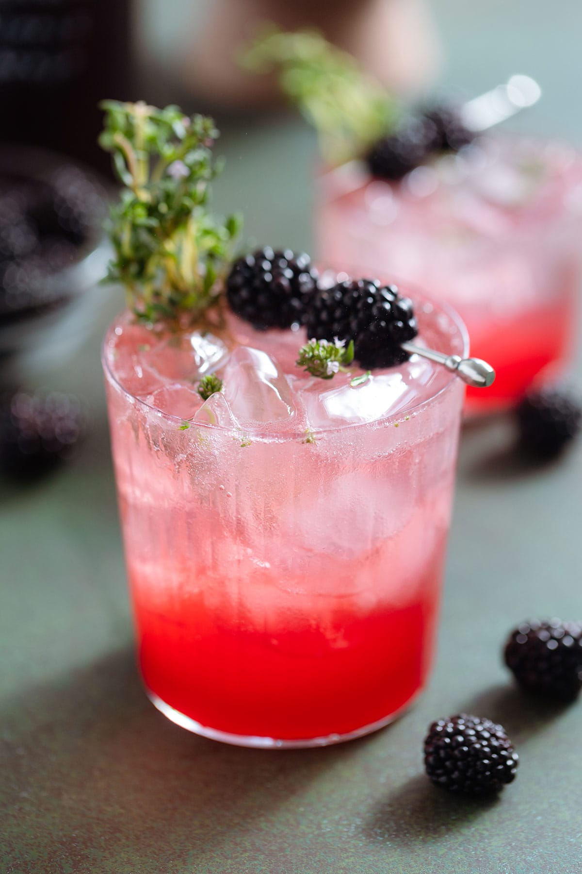 Bright red blackberry mocktail with seltzer on top creating an ombre effect in a short glass garnished with blackberries and fresh thyme.