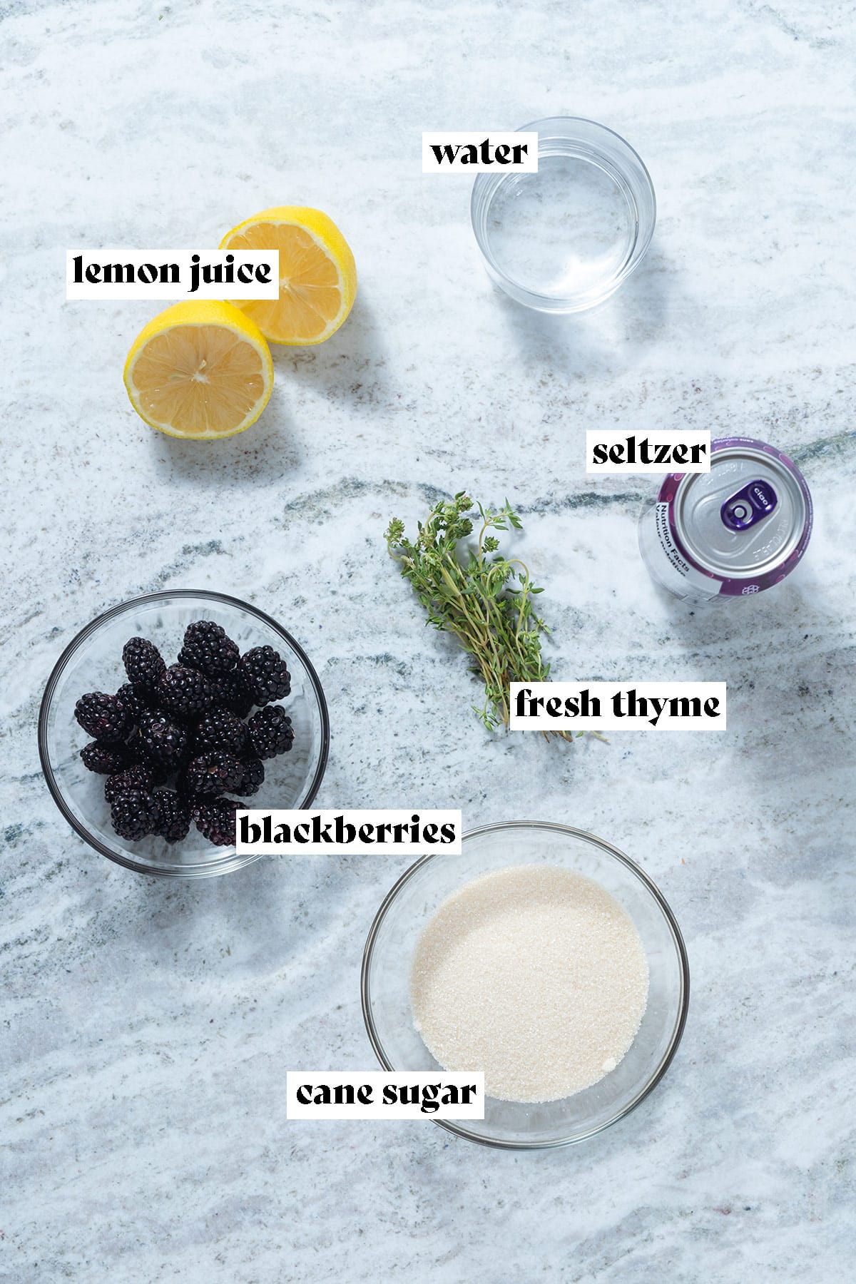 Ingredients like blackberries, lemon, thyme, and sugar laid out on a grey stone background.