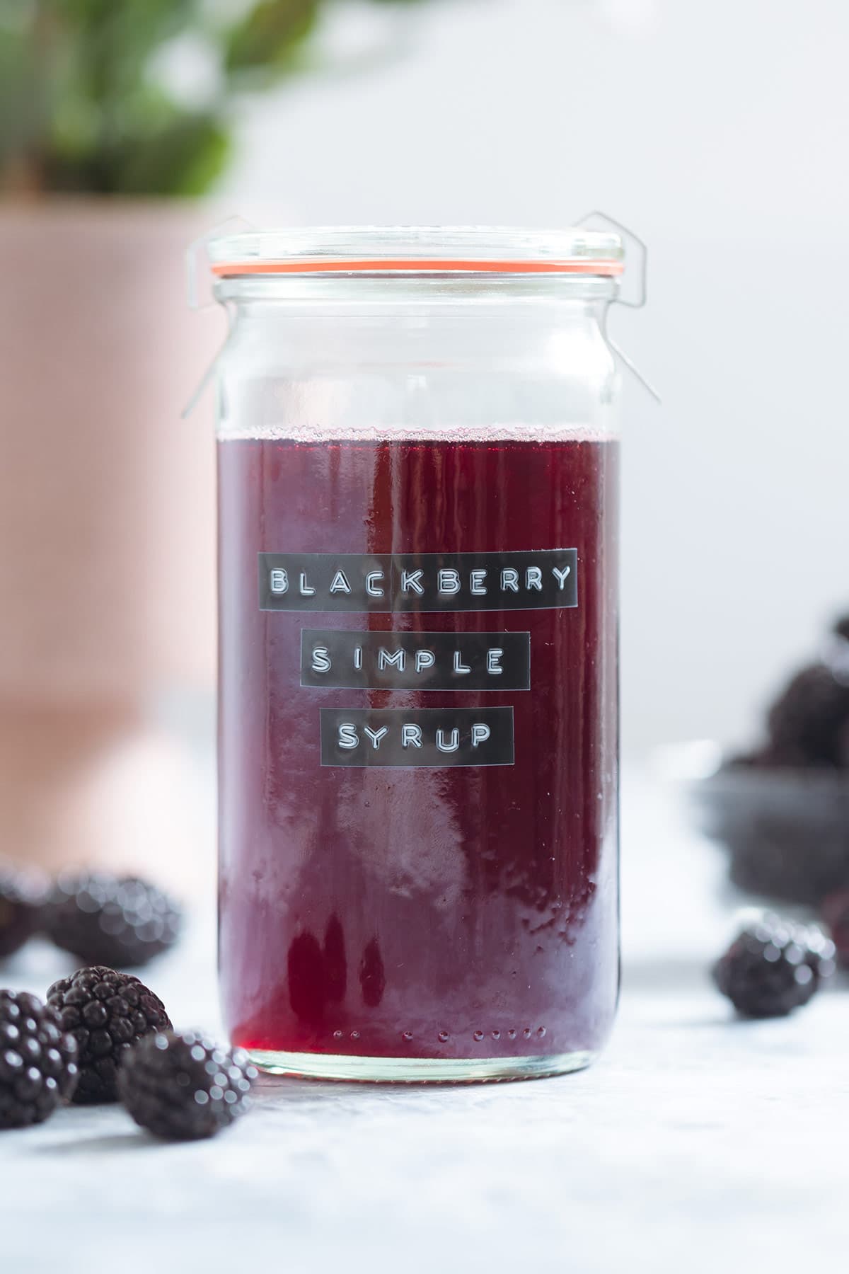 A glass jar with blackberry simple syrup with fresh blackberries around the jar.