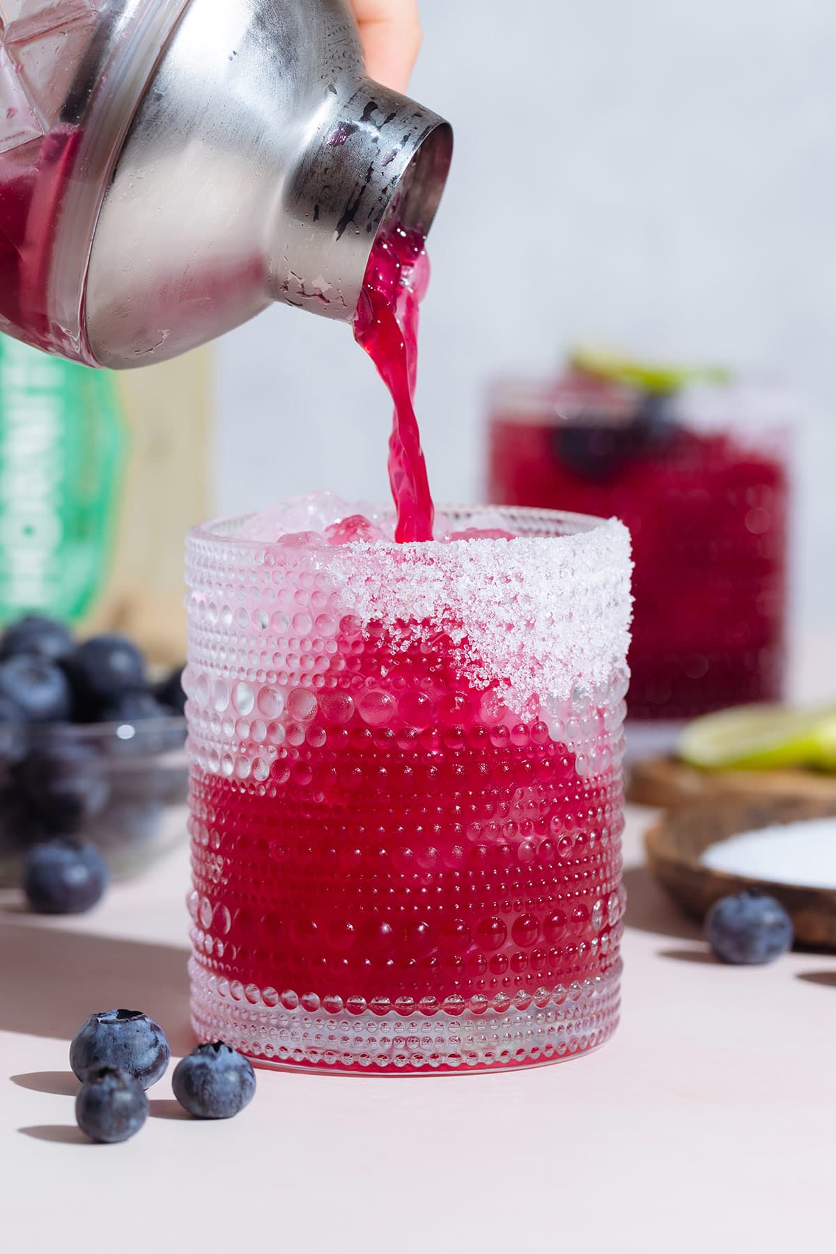 Bright pink purple margarita being poured into a short glass from a glass cocktail shaker.
