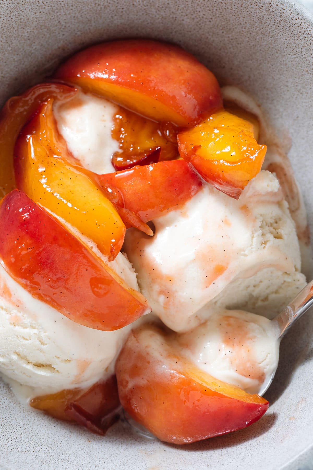 Caramelized peaches with vanilla ice cream in a grey bowl with a spoon.