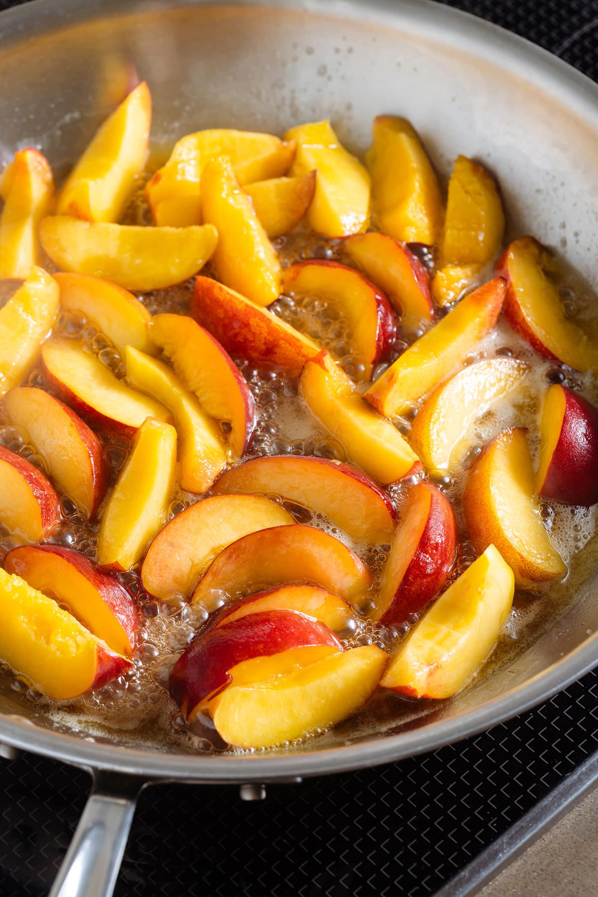 Sliced peaches cooking in a large pan with butter and maple syrup.