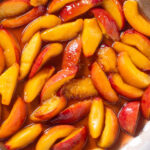 Caramelized sliced peaches with maple syrup in a steel pan.