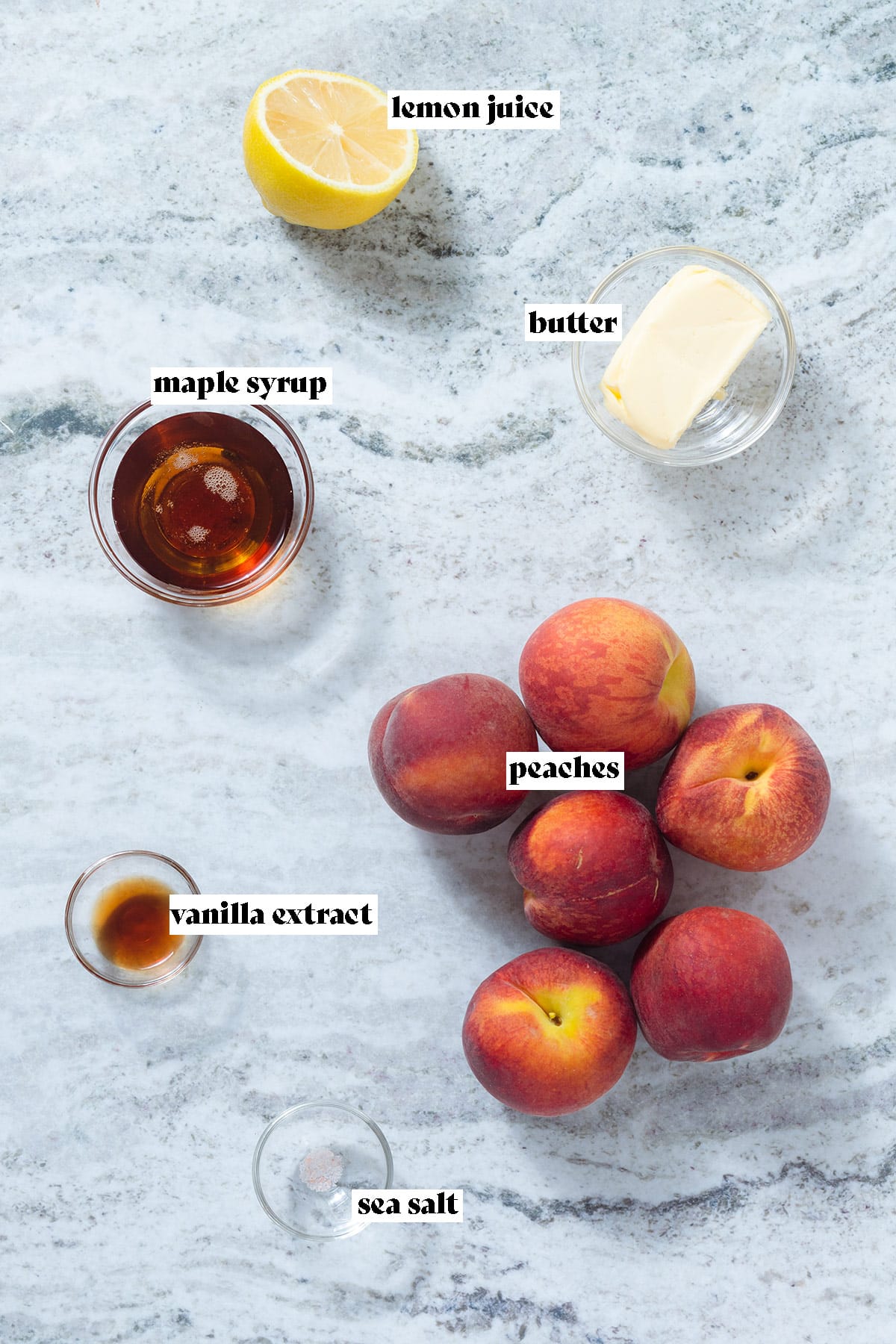 Peaches, maple syrup, lemon, butter, and other ingredients on a grey stone background.