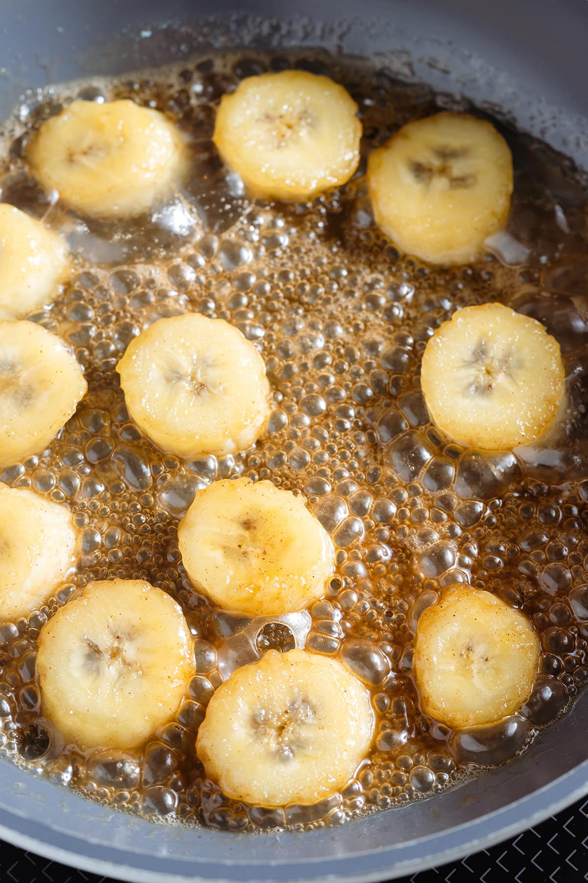 Banana slicing simmering with butter and maple syrup in a non-stick pan.