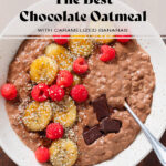 Chocolate oatmeal in a beige bowl topped with fresh raspberries, caramelized banana slices and chocolate squares.