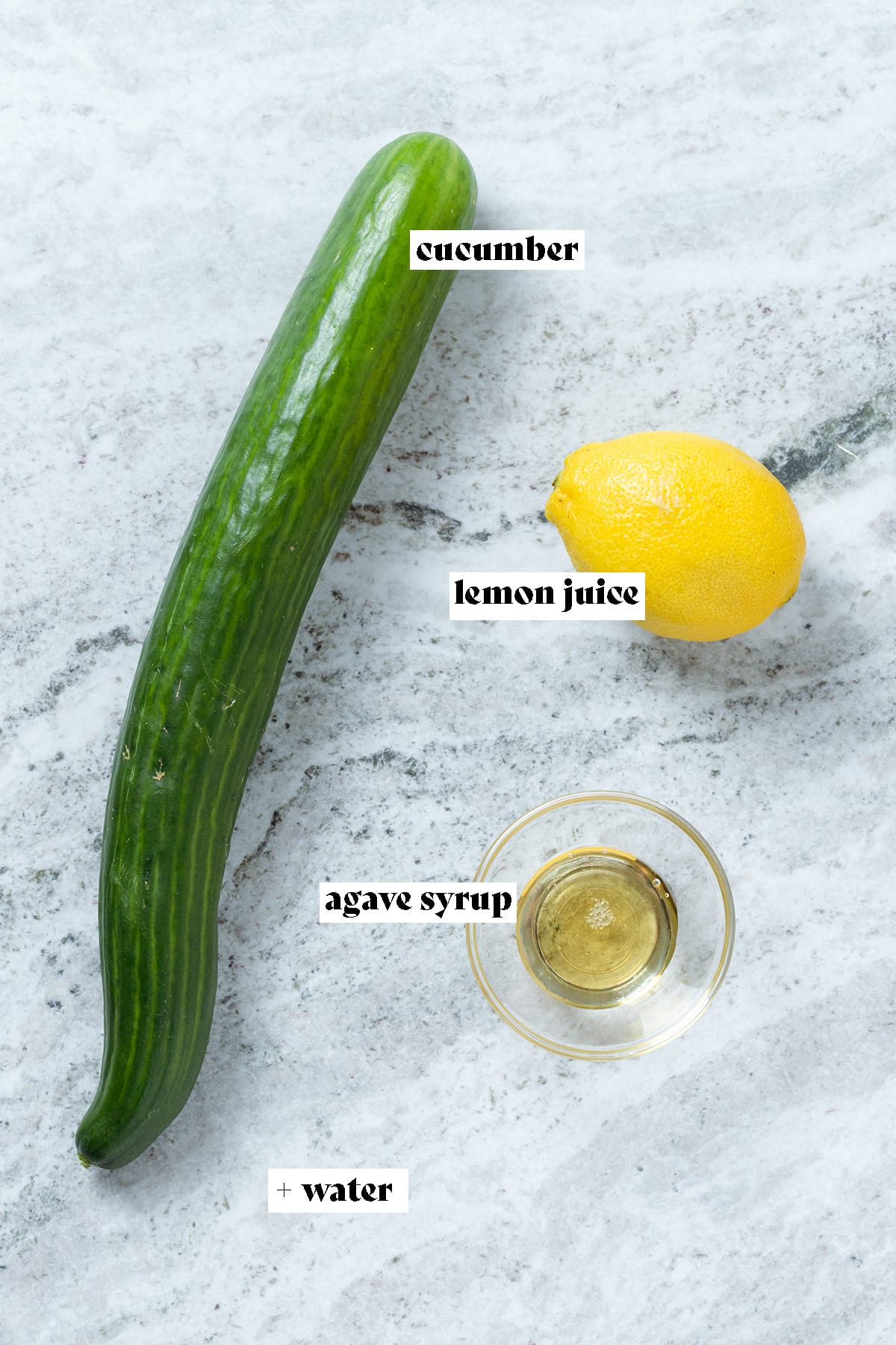 Cucumber, lemon, and agave syrup laid out on a grey stone background with text overlay.
