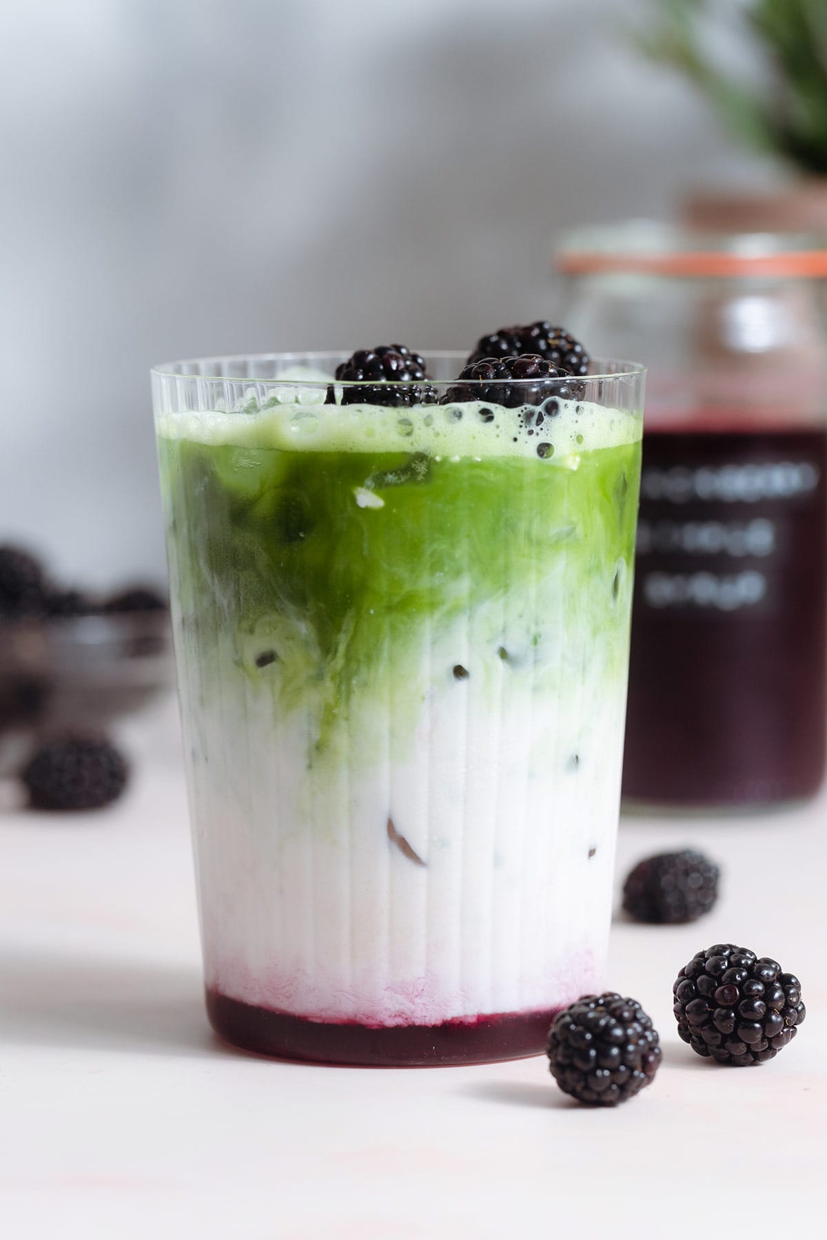 Matcha latte with three layers of matcha, milk, and blackberry syrup in a tall glass garnished with blackberries.