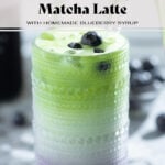 Iced matcha latte in a tall glass with a layer of blueberry syrup on the bottom of the glass garnished with fresh blueberries.