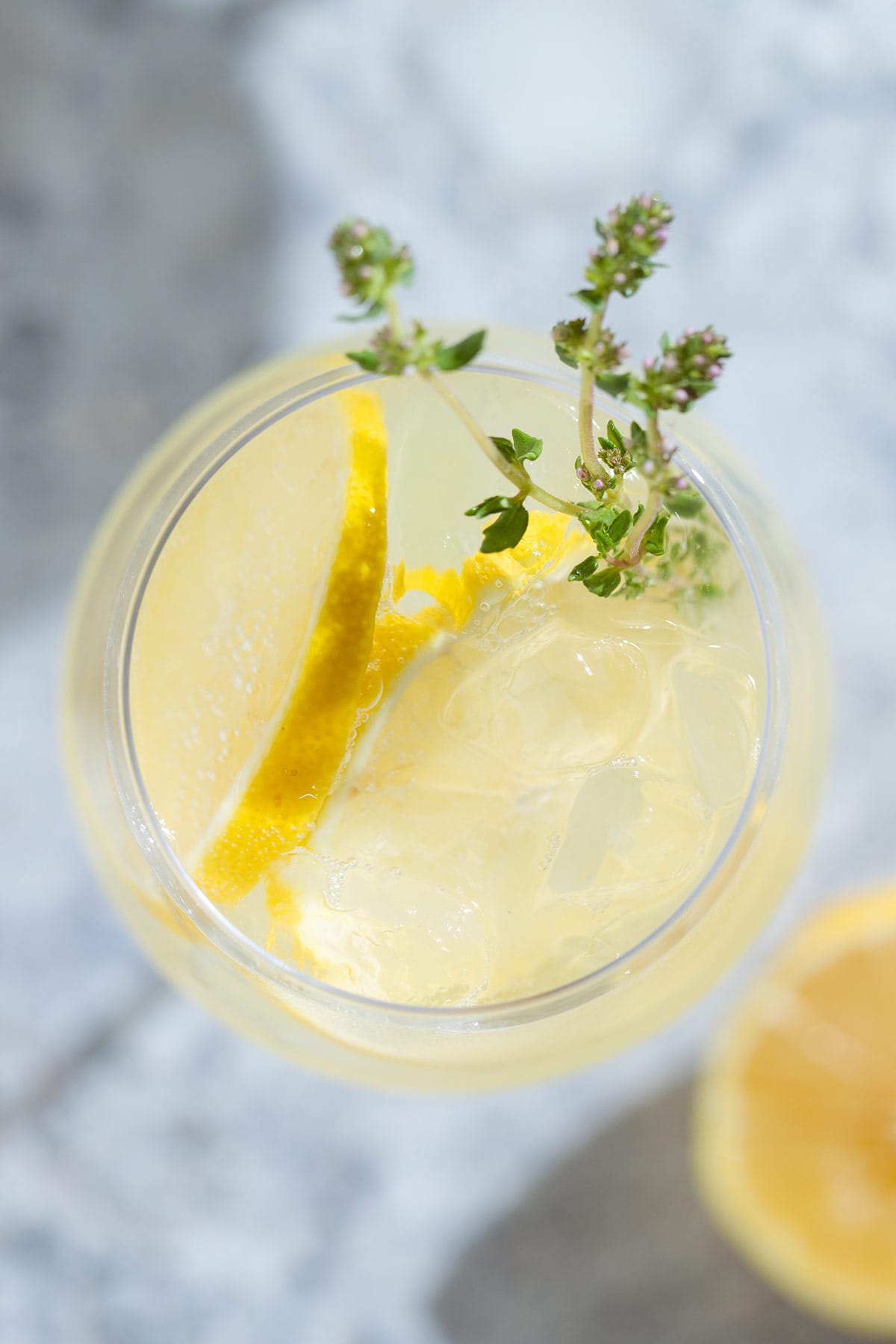 A tall white wine glass with a lemon spritzer garnished with lemon slices and fresh thyme.