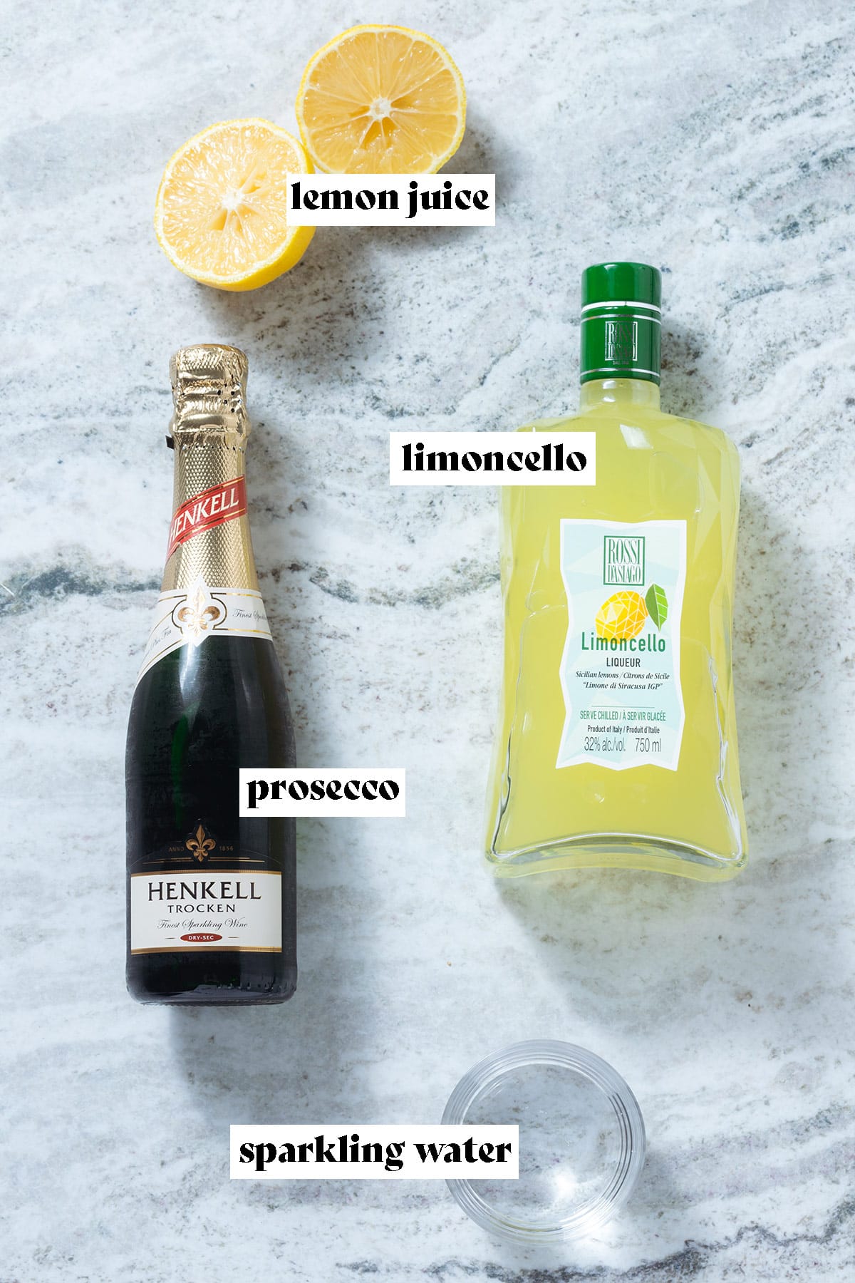 Prosecco, limoncello, lime, and seltzer laid out on a grey stone background.