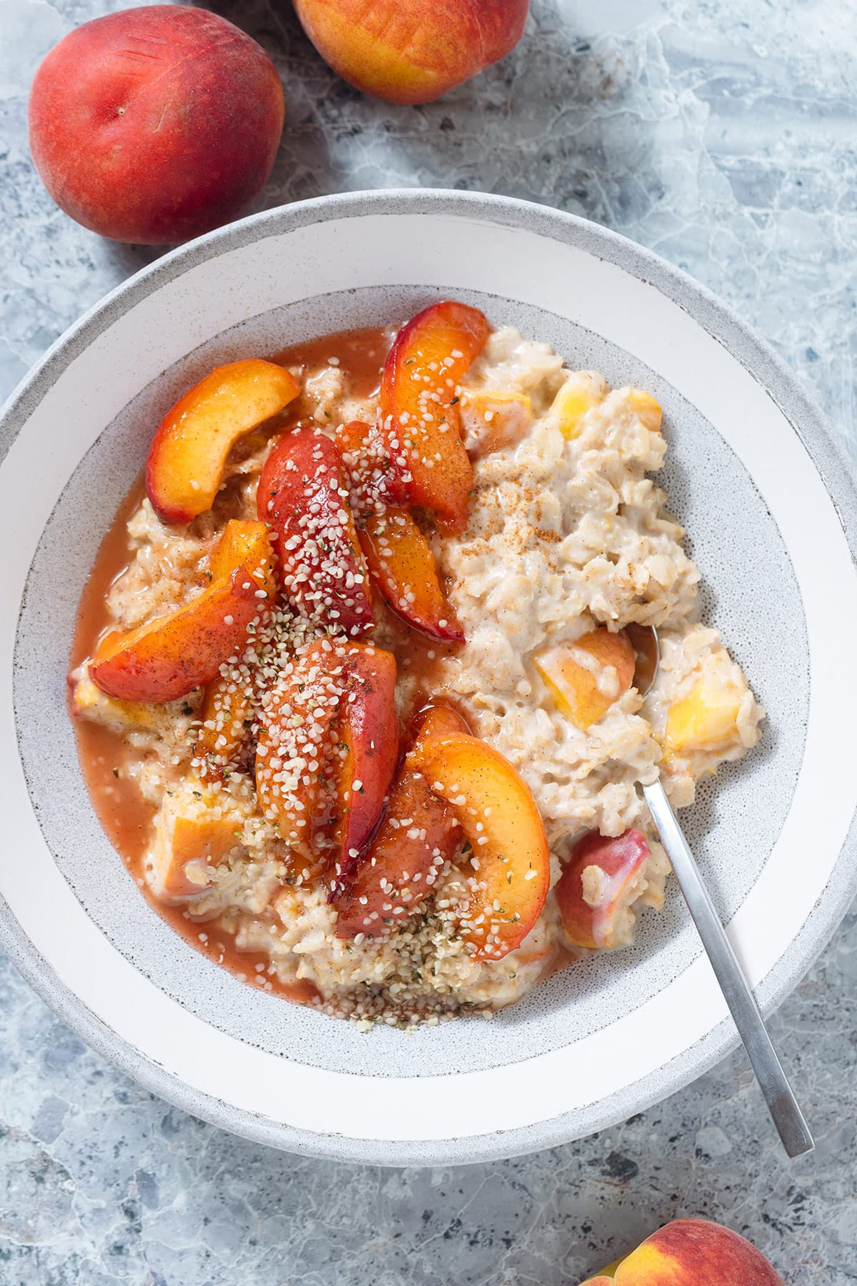 Peach oatmeal with caramelized peaches and hemp seeds on top in a a grey bowl.