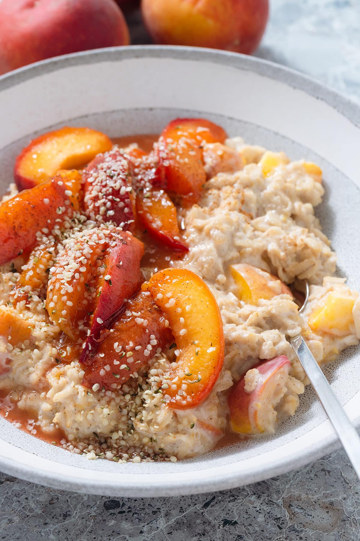 Creamy peach oatmeal with caramelized peaches and hemp seeds on top in a a grey bowl.