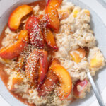 Peach oatmeal with caramelized peaches and hemp seeds on top in a a grey bowl.