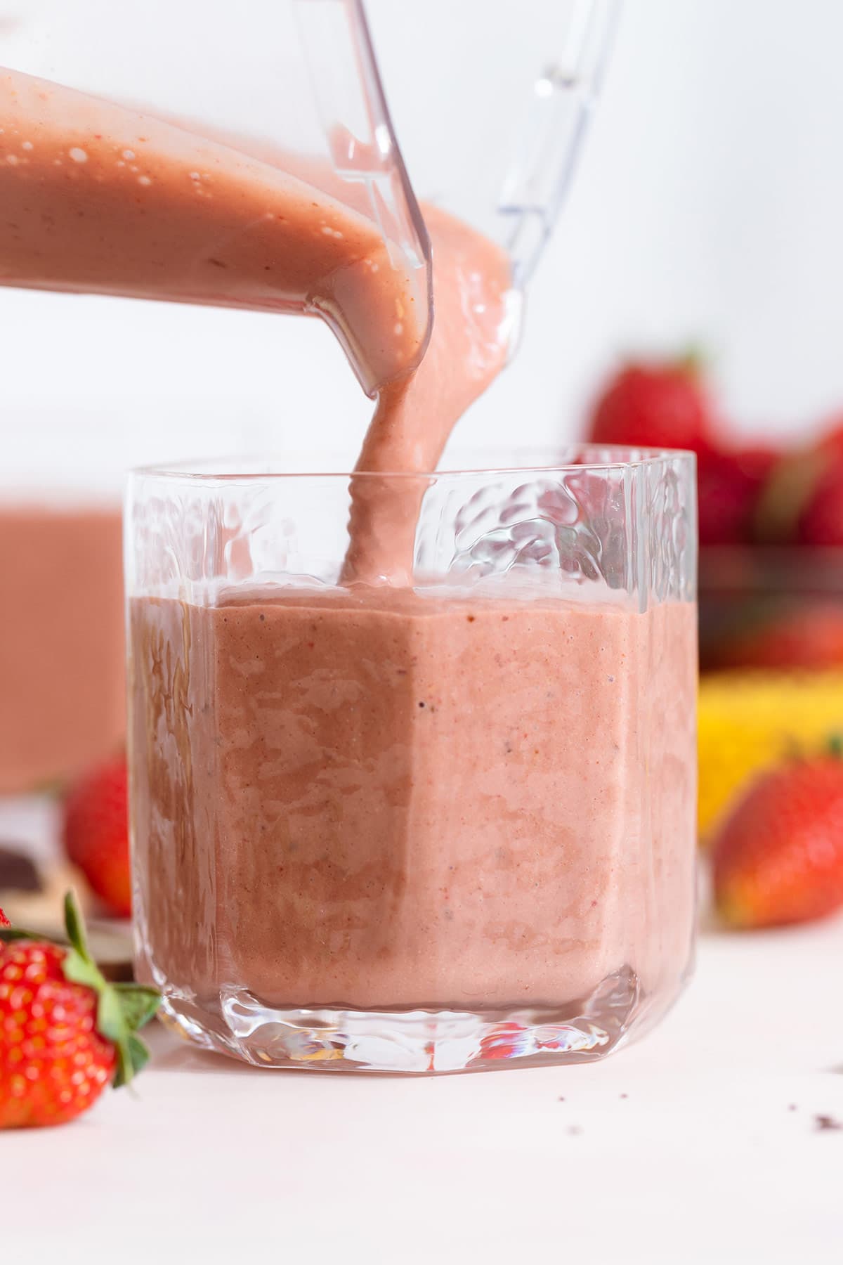 Strawberry smoothie being poured into a short glass on a white background.