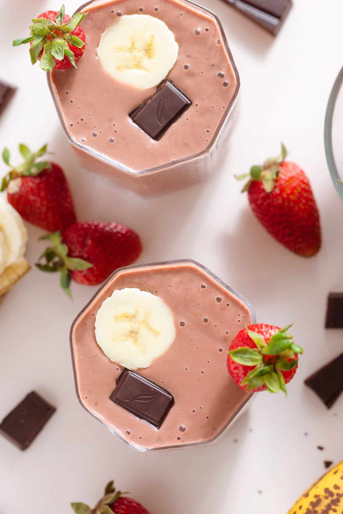 Strawberry smoothie in a short glass garnished with a strawberry, a banana slice, and a square of chocolate.