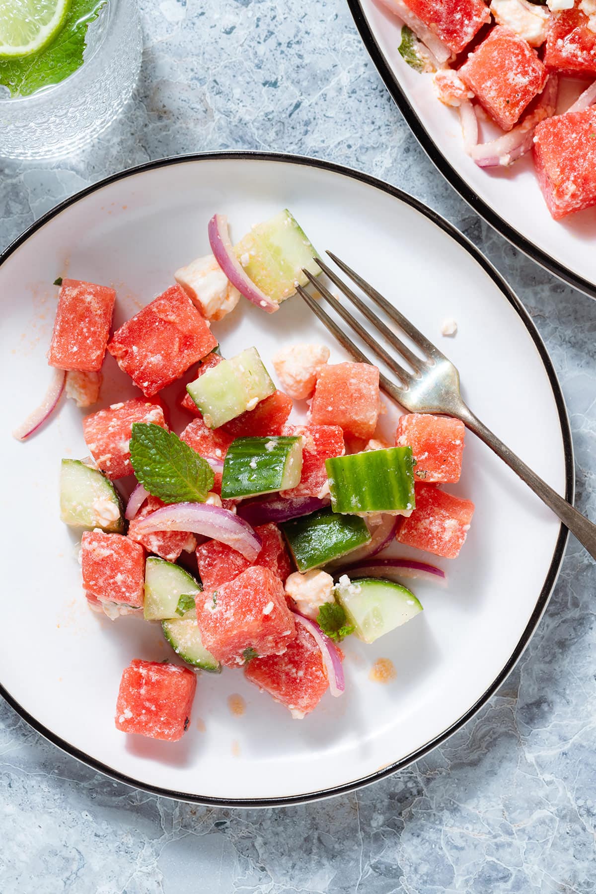 Watermelon salad on a small white salad plate with a black with a silver fork on the right side of the plate.