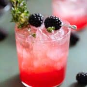 Bright red blackberry mocktail with seltzer on top creating an ombre effect in a short glass garnished with blackberries and fresh thyme.