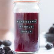 A glass jar with blackberry simple syrup with fresh blackberries around the jar.