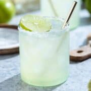 Classic margarita in a short glass with a golden straw garnished a slice of lime.
