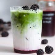 Matcha latte with three layers of matcha, milk, and blackberry syrup in a tall glass garnished with blackberries.