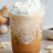 A plastic Starbucks cup with iced mocha over ice garnished with whipped cream and melted white chocolate.