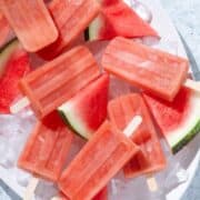 Watermelon popsicles on a large white serving platter with ice and slices of watermelon.