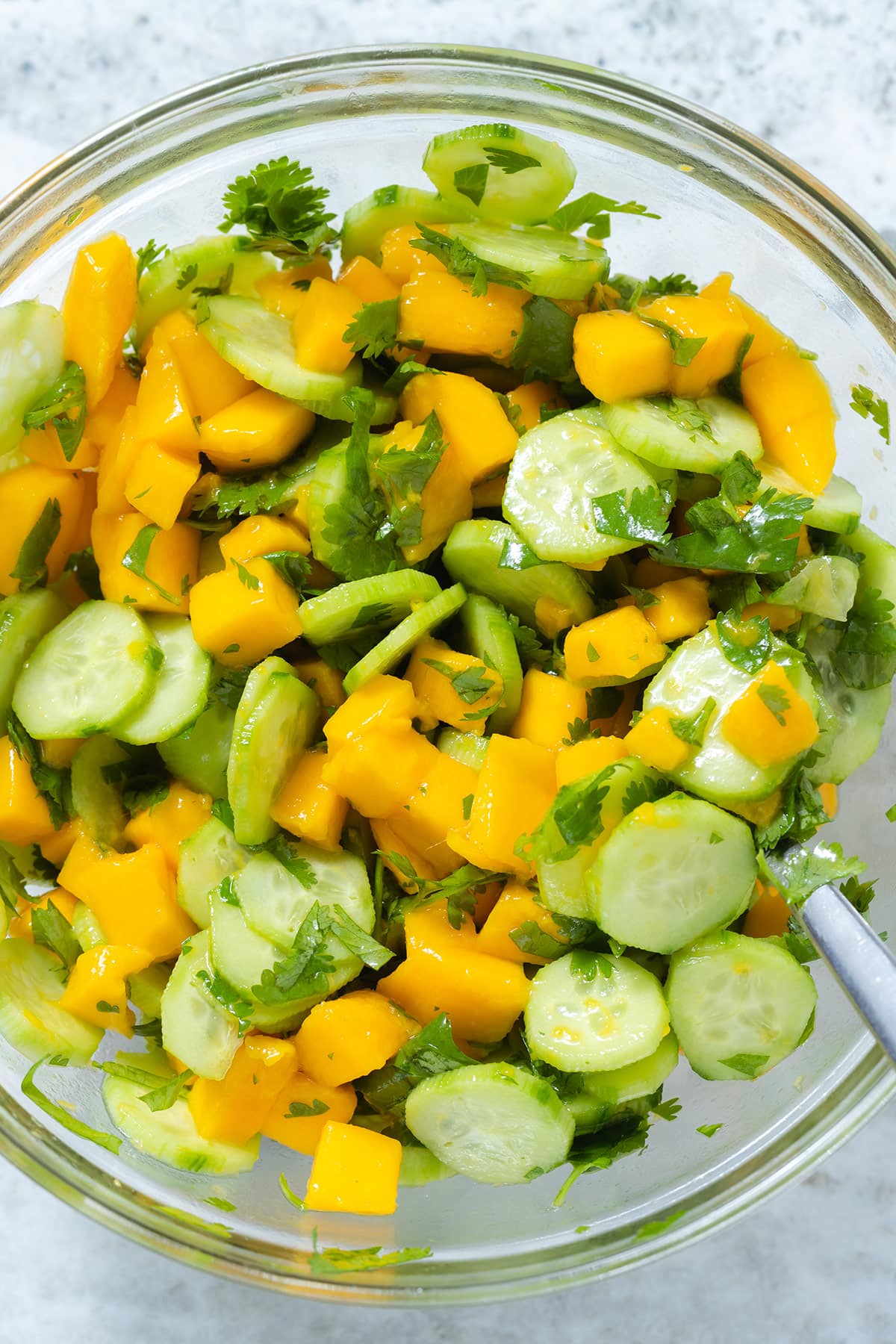 Mango and cucumber salad with fresh cilantro and sesame seeds in a glass bowl with a white rim.