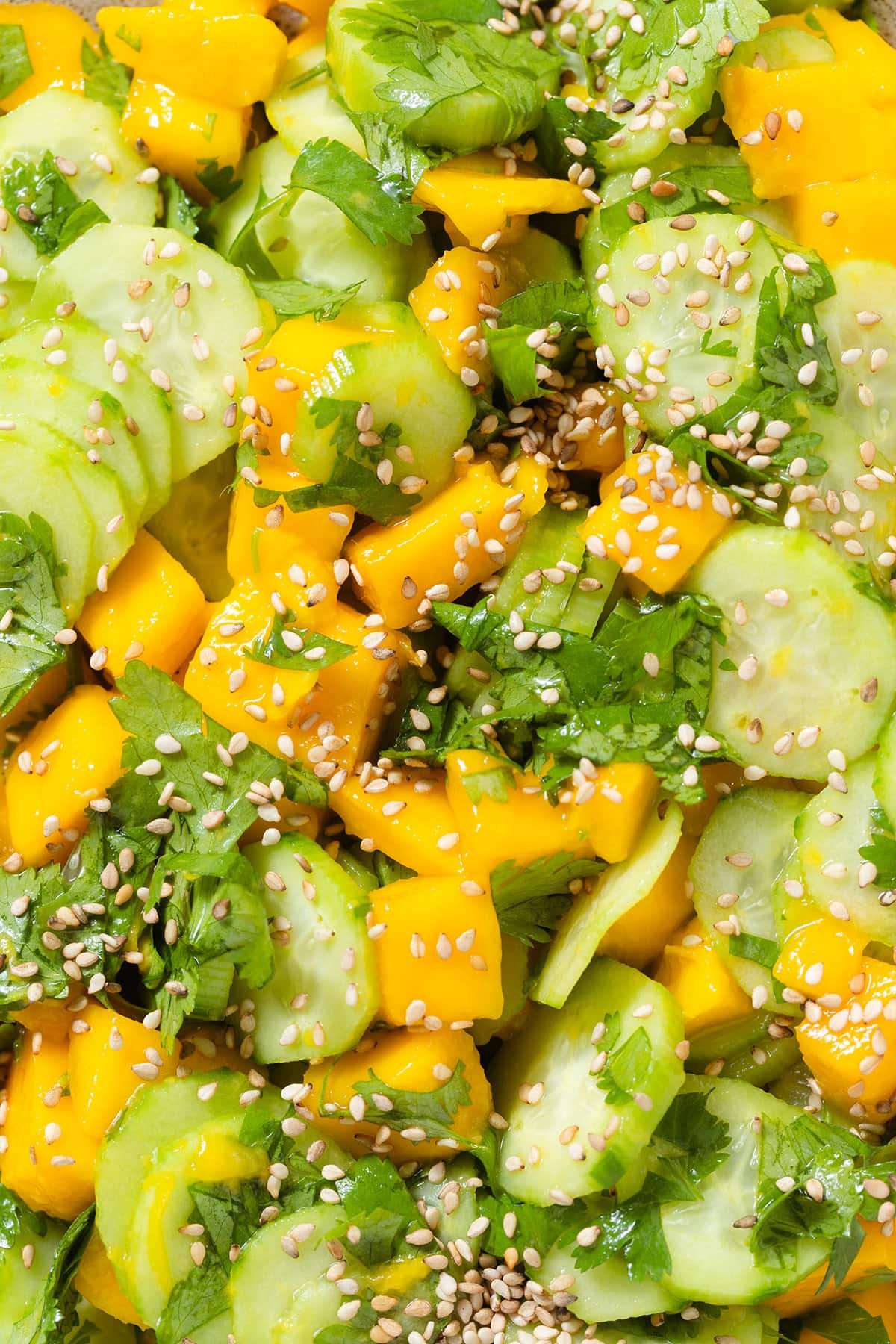 A close up of mango and cucumber salad with fresh cilantro and sesame seeds.