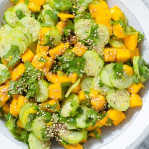 Mango and cucumber salad with fresh cilantro and sesame seeds in a grey ceramic bowl with a white rim.