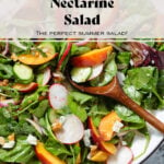 Nectarine salad with mixed greens and radishes on a large white serving platter with a black rim with two wooden spoons inserted in scooping the salad.