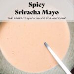 Spicy pale red mayo in a light green striped bowl with a silver spoon inserted into the mayo.