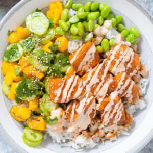 Teriyaki salmon with mango salad, edamame, and rice, in a grey low rim bowl on a grey background.