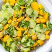 Mango and cucumber salad with fresh cilantro and sesame seeds in a grey ceramic bowl with a white rim.
