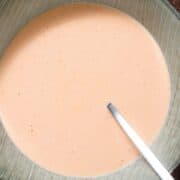 Spicy pale red mayo in a light green striped bowl with a silver spoon inserted into the mayo.