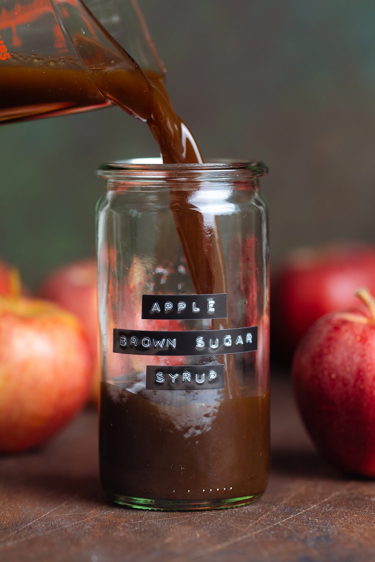 Dark brown syrup being poured into a glass jar with a label on it that says Apple Brown Sugar Syrup.