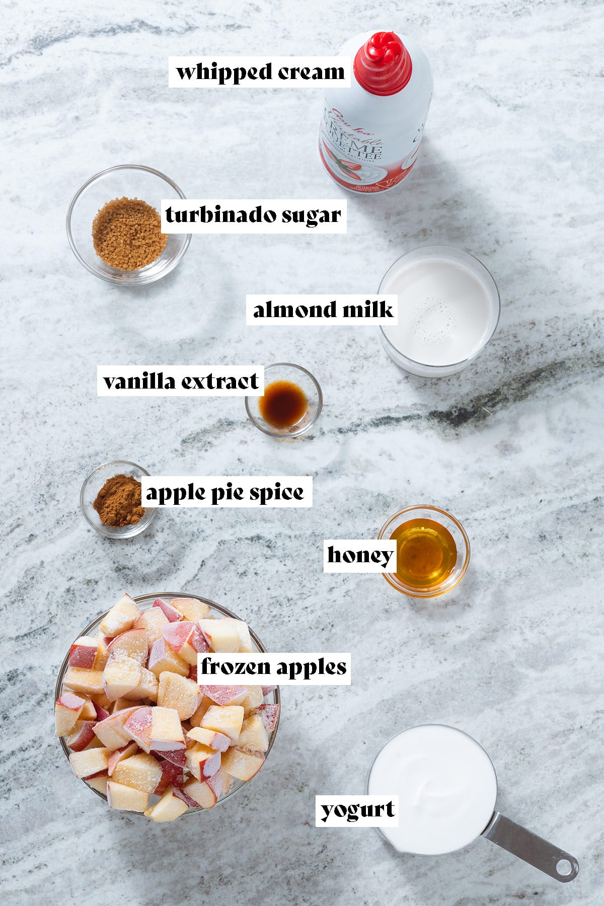 Frozen apples, yogurt, milk, spices, and other ingredients laid out on a grey stone background with text overlay.