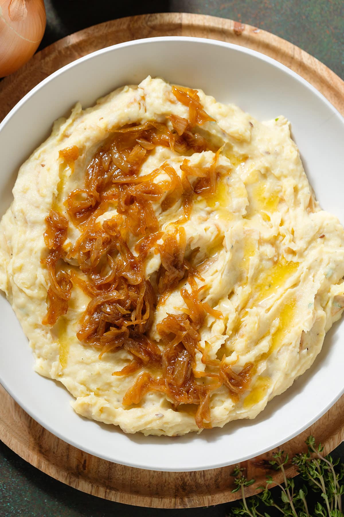 Mashed potatoes topped with caramelized onions in a white bowl on a wooden plate.