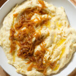 Mashed potatoes topped with caramelized onions in a white bowl.