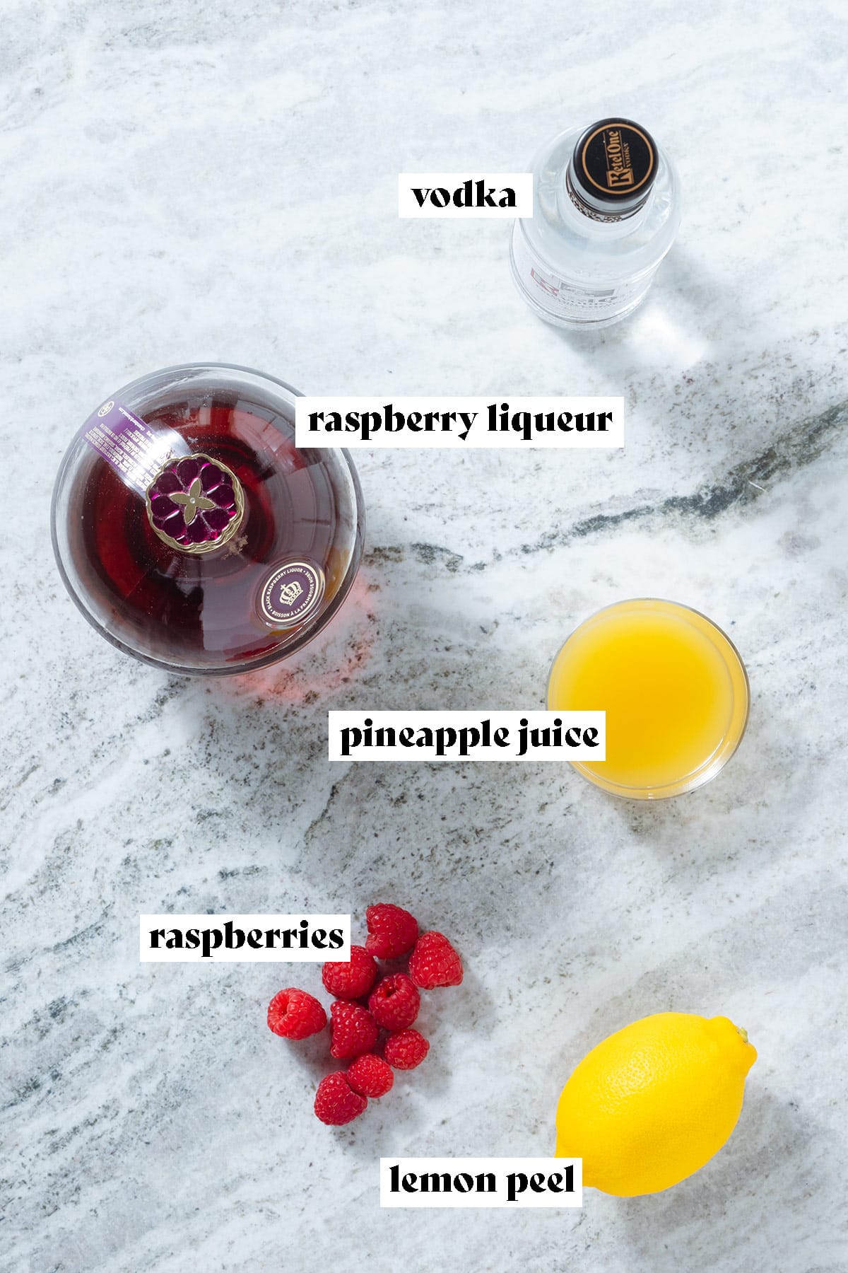 A bottle of vodka, Chambord, a glass of pineapple juice, raspberries, and a lemon on a grey stone background with text overlay.