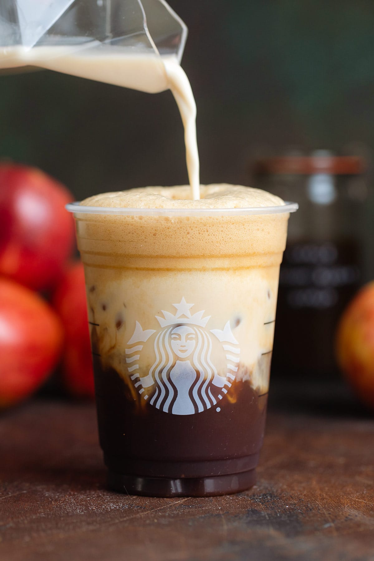 Oat milk being poured into shaken espresso in a plastic Starbucks cup.