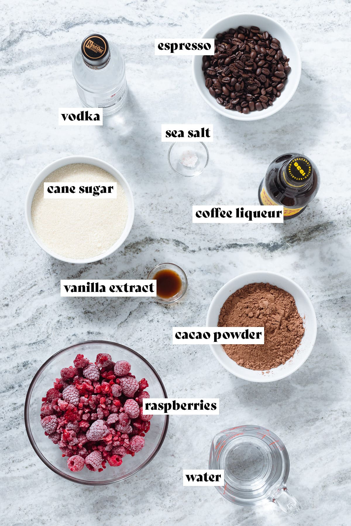 Raspberries, cacao powder, cane sugar, espresso, kahlua, and other ingredients laid out on a grey stone background with text overlay.