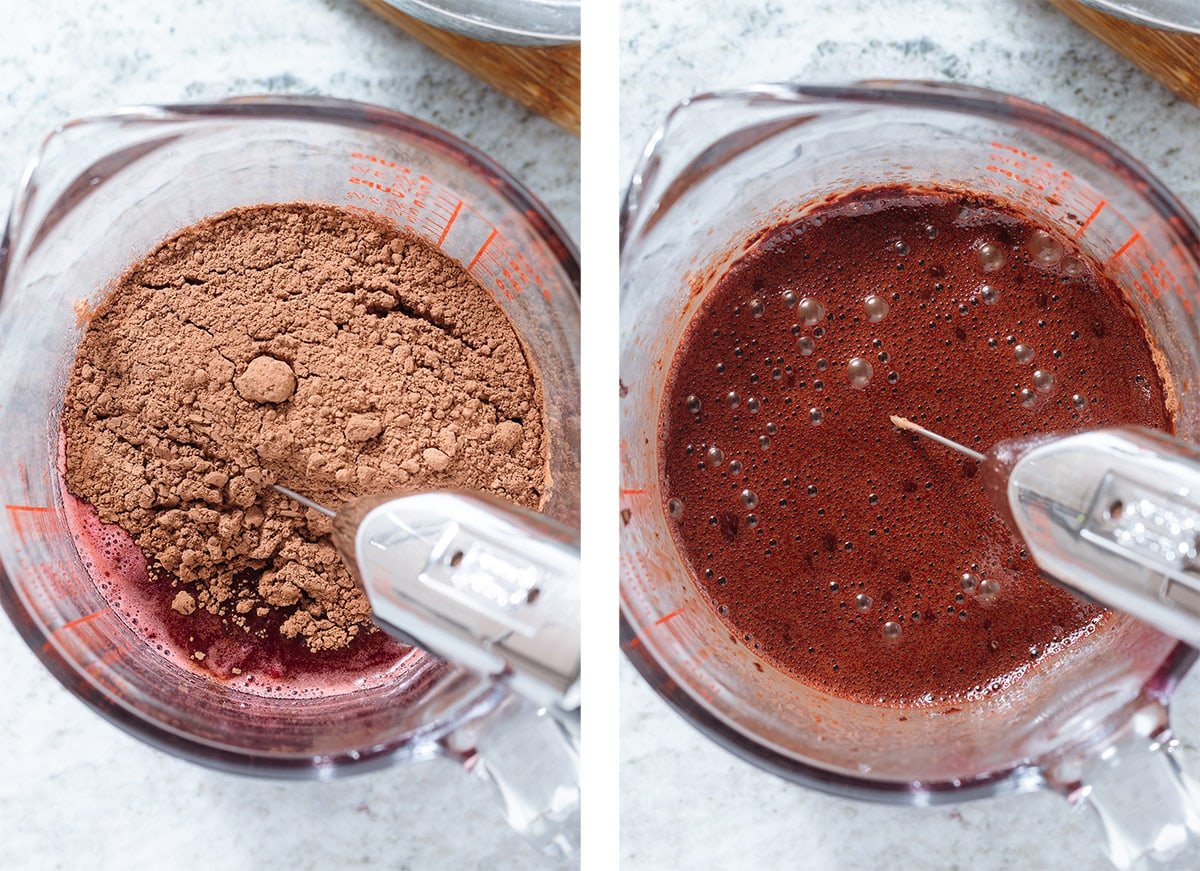 Cacao powder being mixed into raspberry syrup in a large glass measuring cup with a handheld milk frother.