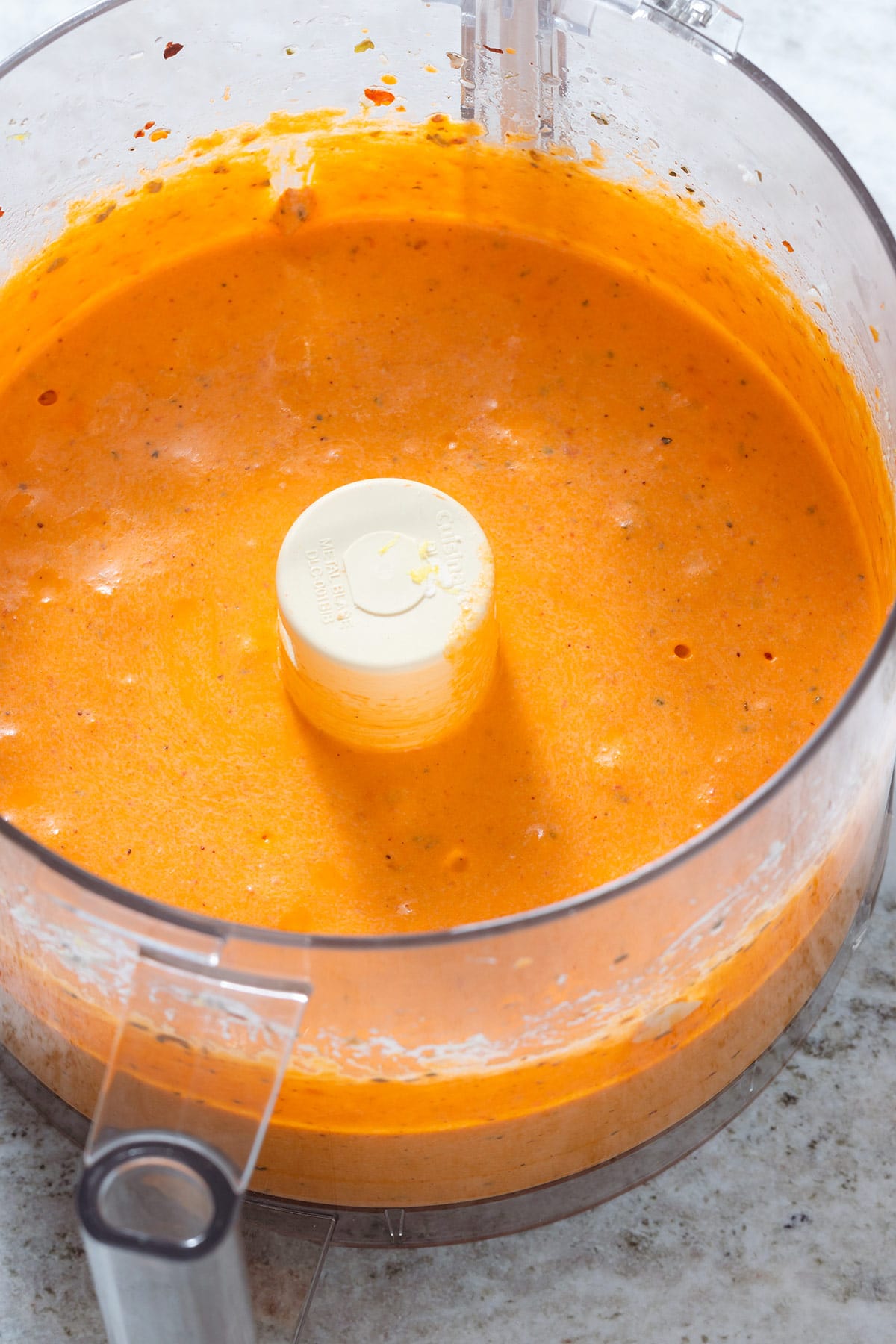 Bright orange feta dip in a food processor on a grey stone background.