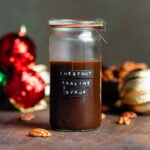 Dark brown chestnut praline syrup in a glass jar with a glass lid and a black label with the name of the syrup on the side of the glass.
