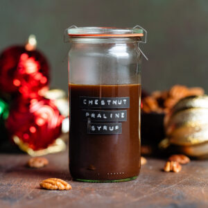 Dark brown chestnut praline syrup in a glass jar with a glass lid and a black label with the name of the syrup on the side of the glass.