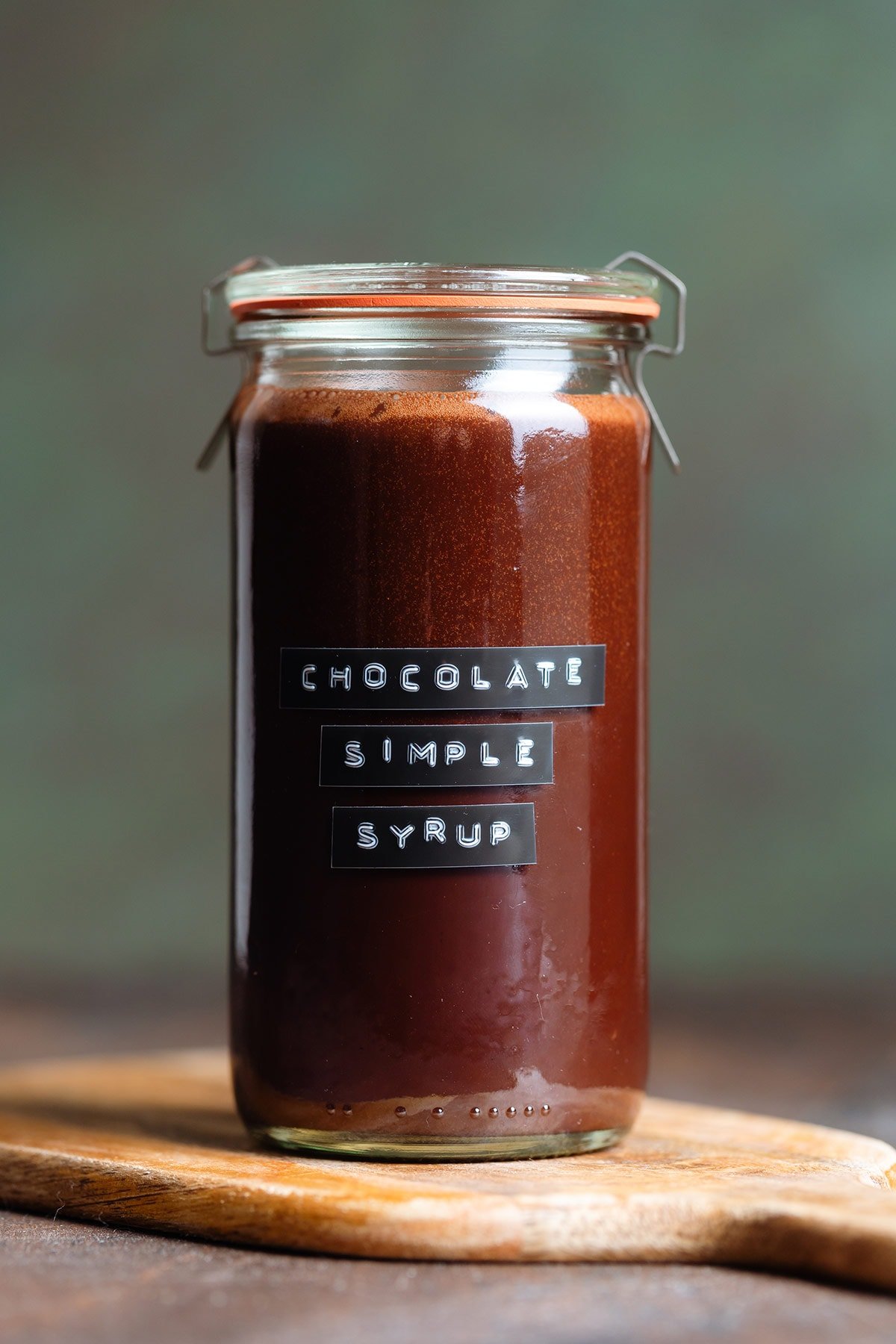 Chocolate syrup in a glass jar with a black and white embossed label on a dark wooden background.