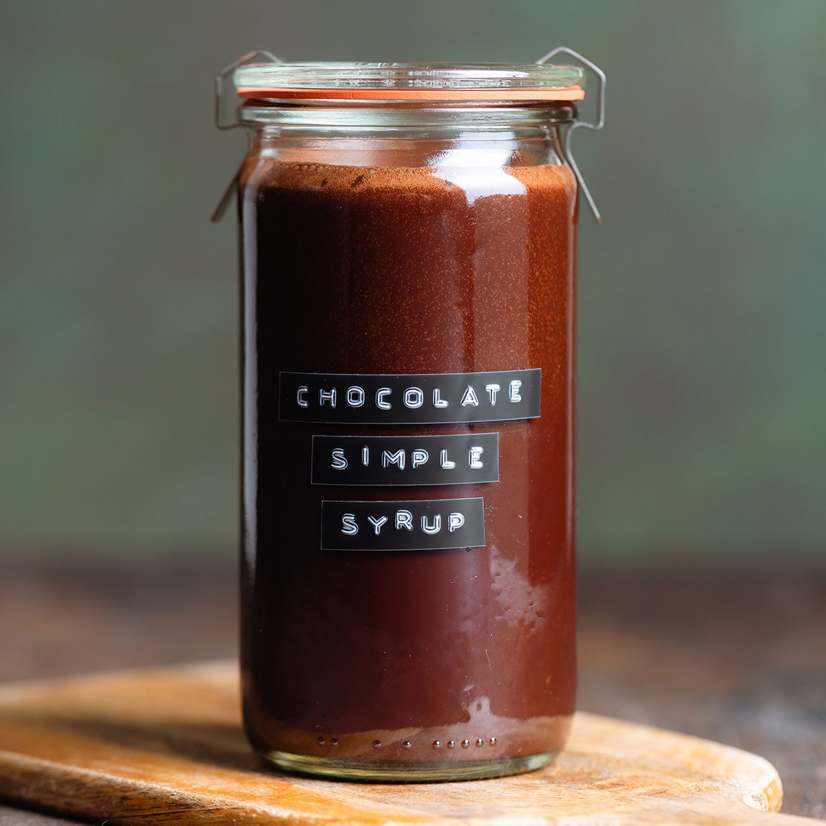 Chocolate syrup in a glass jar with a black and white embossed label on a dark wooden background.